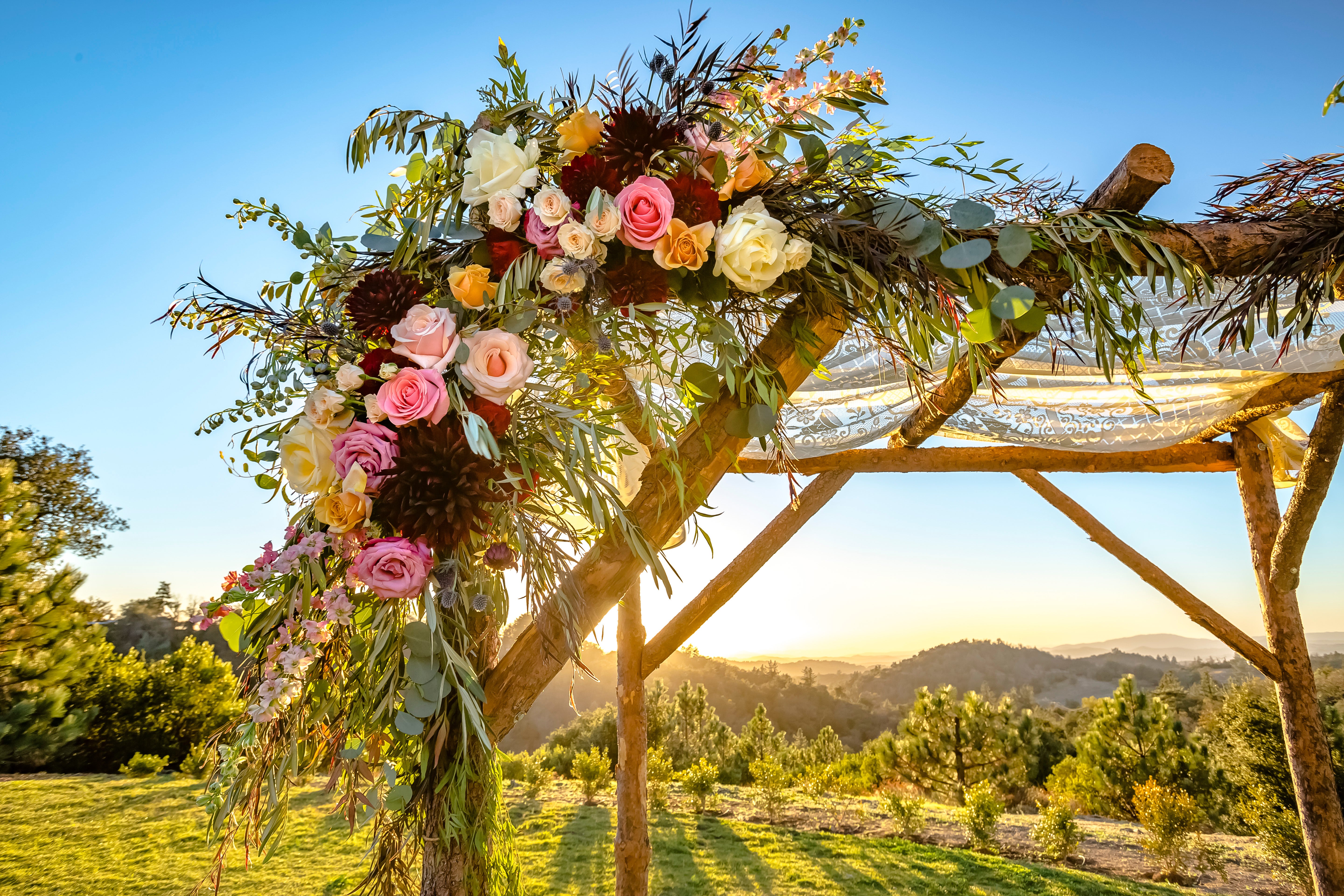 A lush, modern floral arch in deep burgundy and cream tones, with textured blooms and trailing greenery, set against a neutral backdrop.